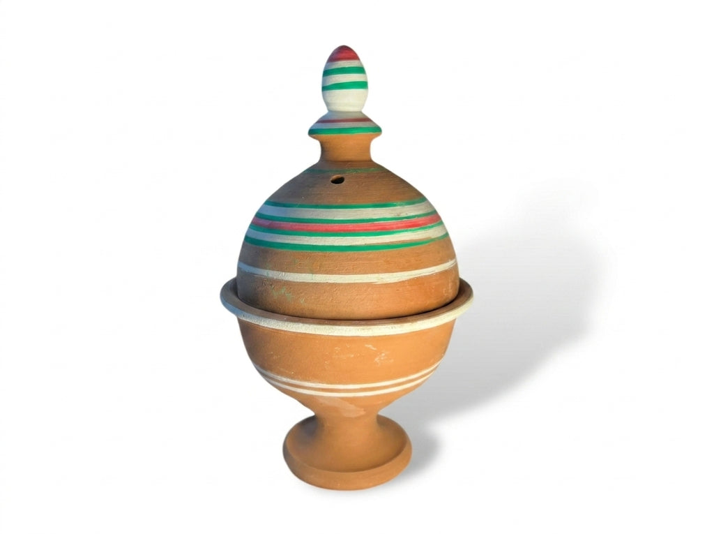 Fumée parfumée de bois de oud s'échappant délicatement des perforations de l'encensoir en argile marocaine.